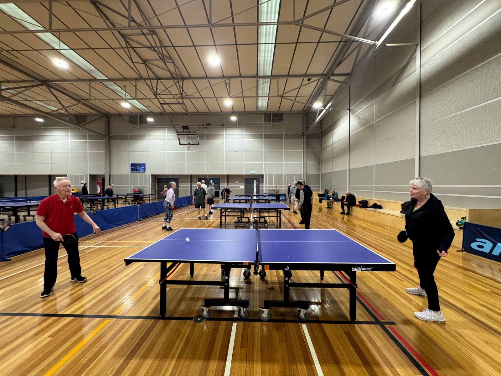 Members playing doubles across several tables in the stadium at Boroondara Sports Complex